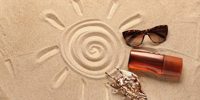 Un dessin de soleil dans le sable, avec des lunettes de soleil et un produit cosmétique